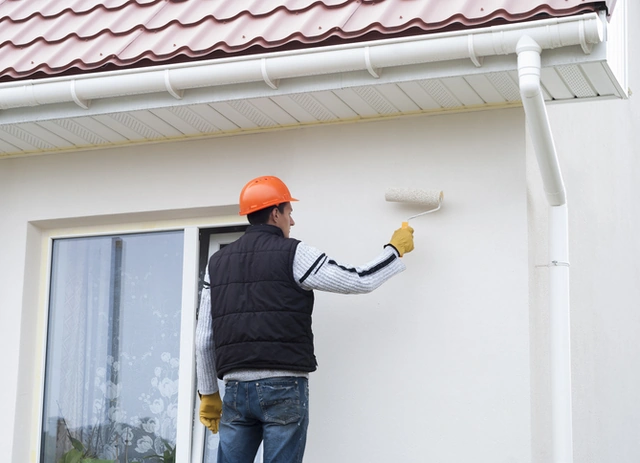 Painter applying paint to the exterior wall of a house